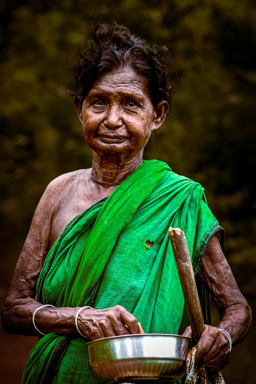 Free A striking portrait of an elderly woman in a vibrant green sari holding a metal bowl outdoors. Stock Photo