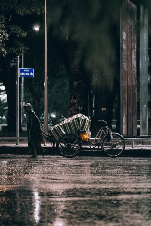 Free Moody urban night scene featuring a bicycle on a rainy street, capturing solitude. Stock Photo