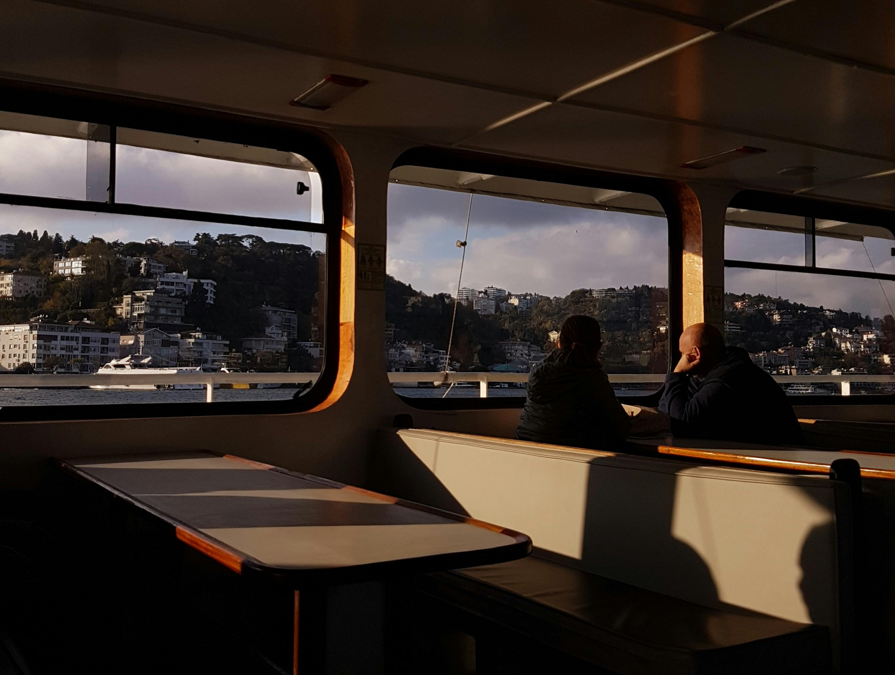 A peaceful scene of two people enjoying a sunset view from a ferry, overlooking a scenic coastline.