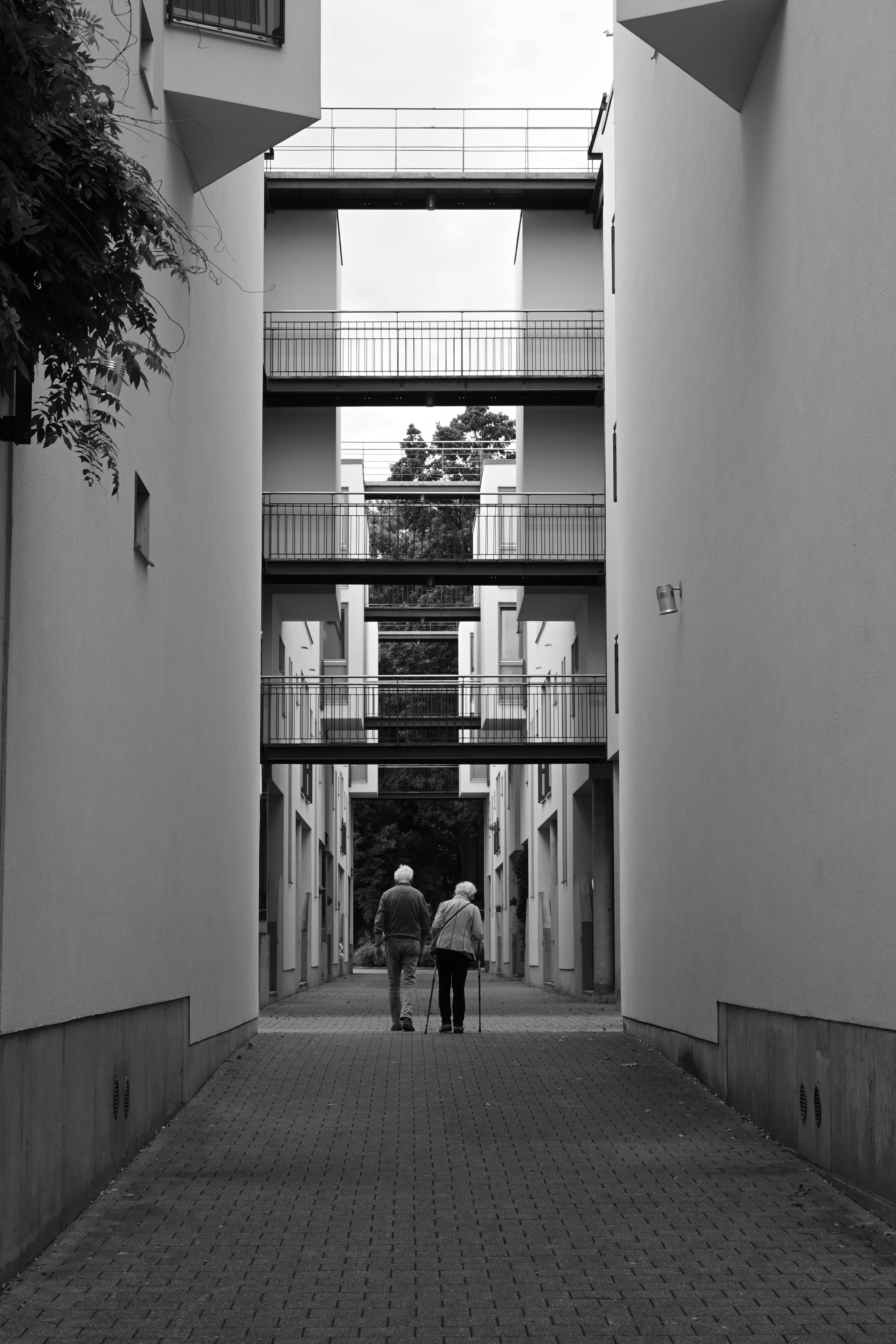 Black and white photo of an elderly couple walking through a modern urban alleyway in Hamburg, Germany.