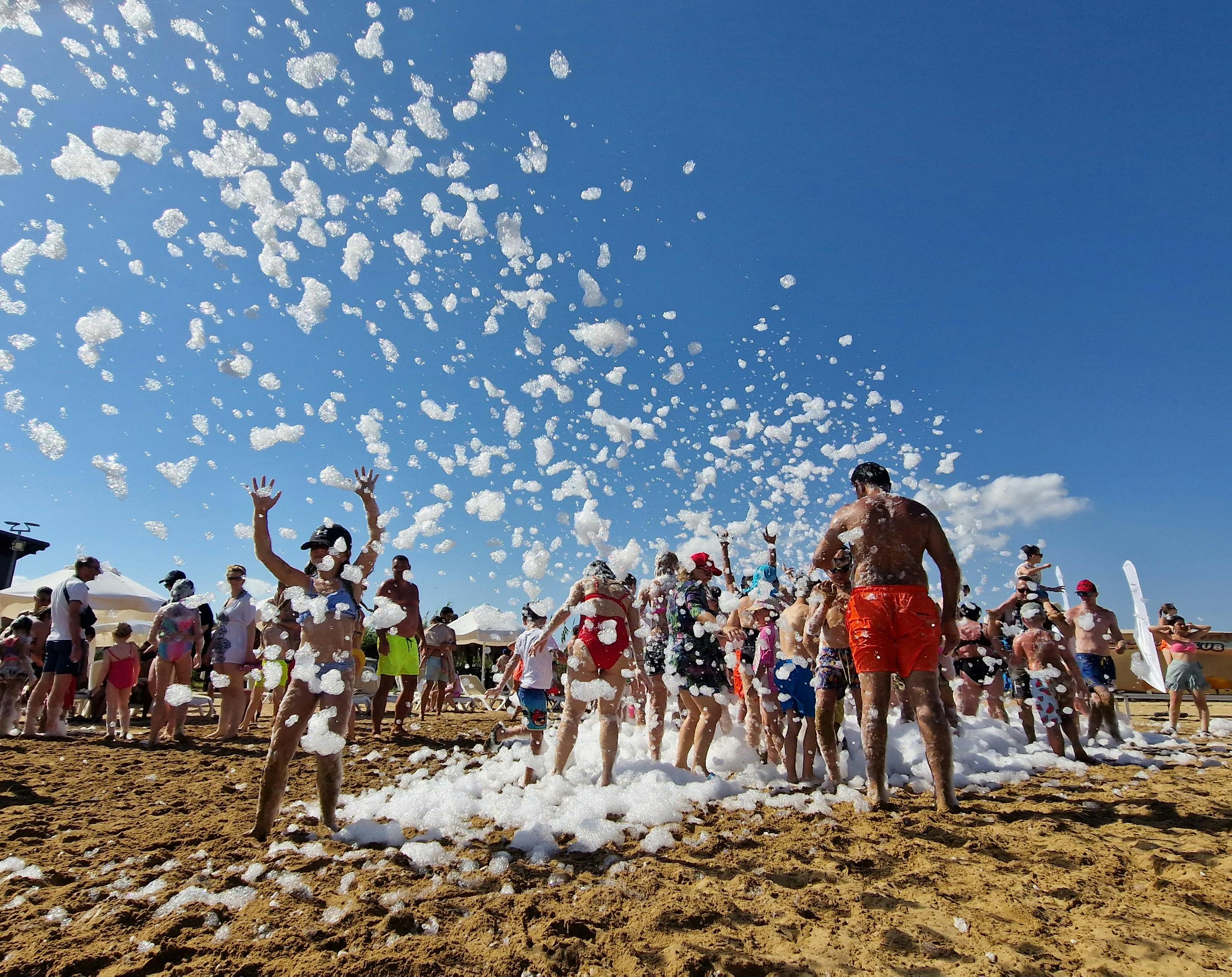 Crowd playing in a foam-filled beach scene under a bright blue sky