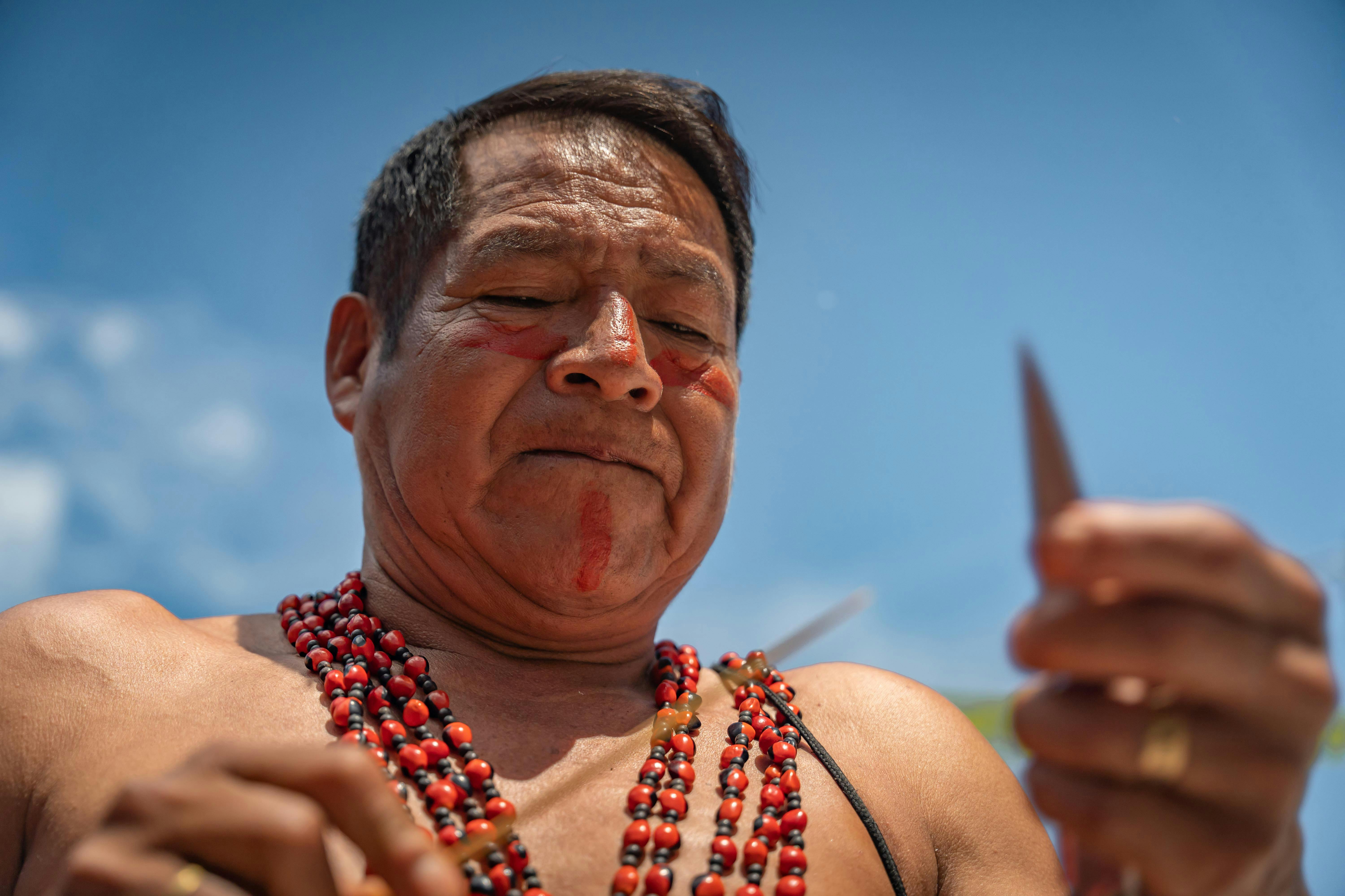 Indigenous elder adorned with bead jewelry, engaging in cultural practices under a clear blue sky.