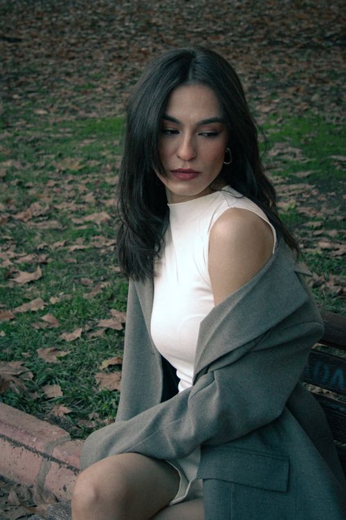 Free Elegant portrait of a woman in fall attire sitting on park bench, surrounded by fallen leaves. Stock Photo