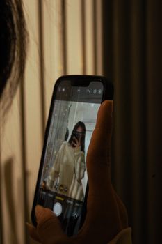 Close-up of a woman holding a smartphone, capturing her reflection in a mirror.