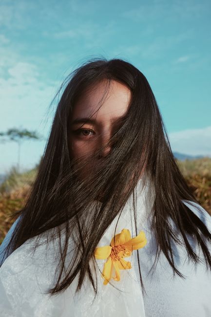 A striking portrait of a woman with long hair and a yellow flower, set against a clear blue sky.