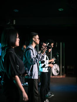 Diverse group of singers performing on stage with microphones in a night setting.