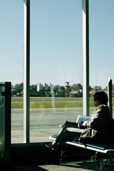 A person sitting in an airport terminal in São Paulo, Brazil, overlooking the runway.