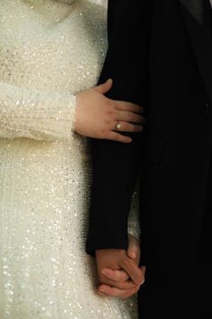 A stylish close-up of a couple holding hands, showcasing a wedding dress and ring.