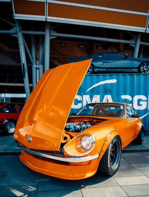 Free Bright vintage orange car with hood open in a vibrant urban scene showcasing automotive design. Stock Photo