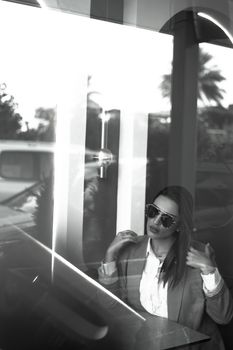 Monochromatic portrait of a stylish woman in sunglasses posing behind reflective glass in Baghdad.