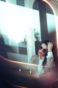 Elegant woman in a suit with sunglasses sitting by a window in Baghdad, Iraq. Modern and chic fashion.