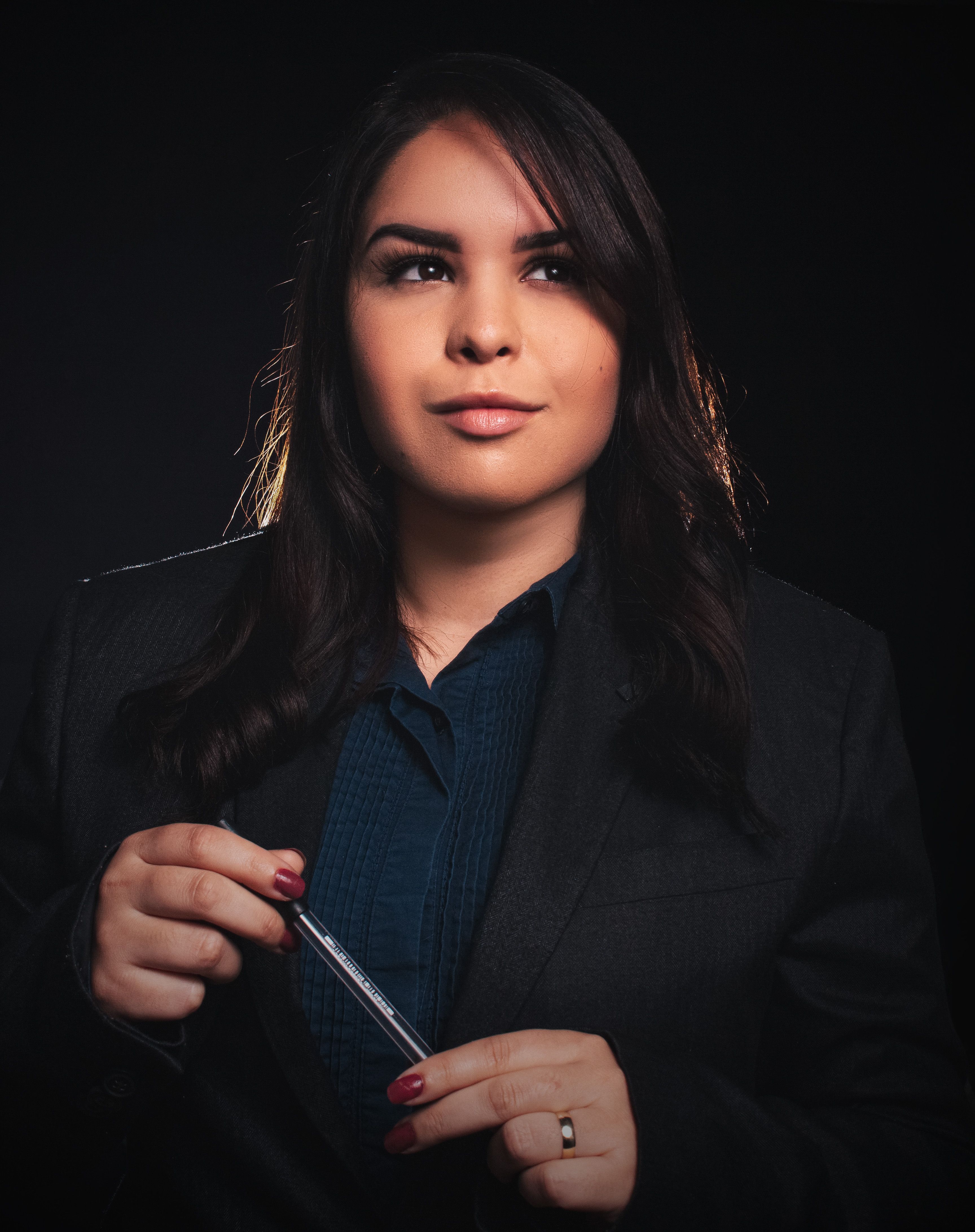 Elegantly posed woman in a studio holding a pen, portraying confidence and style.