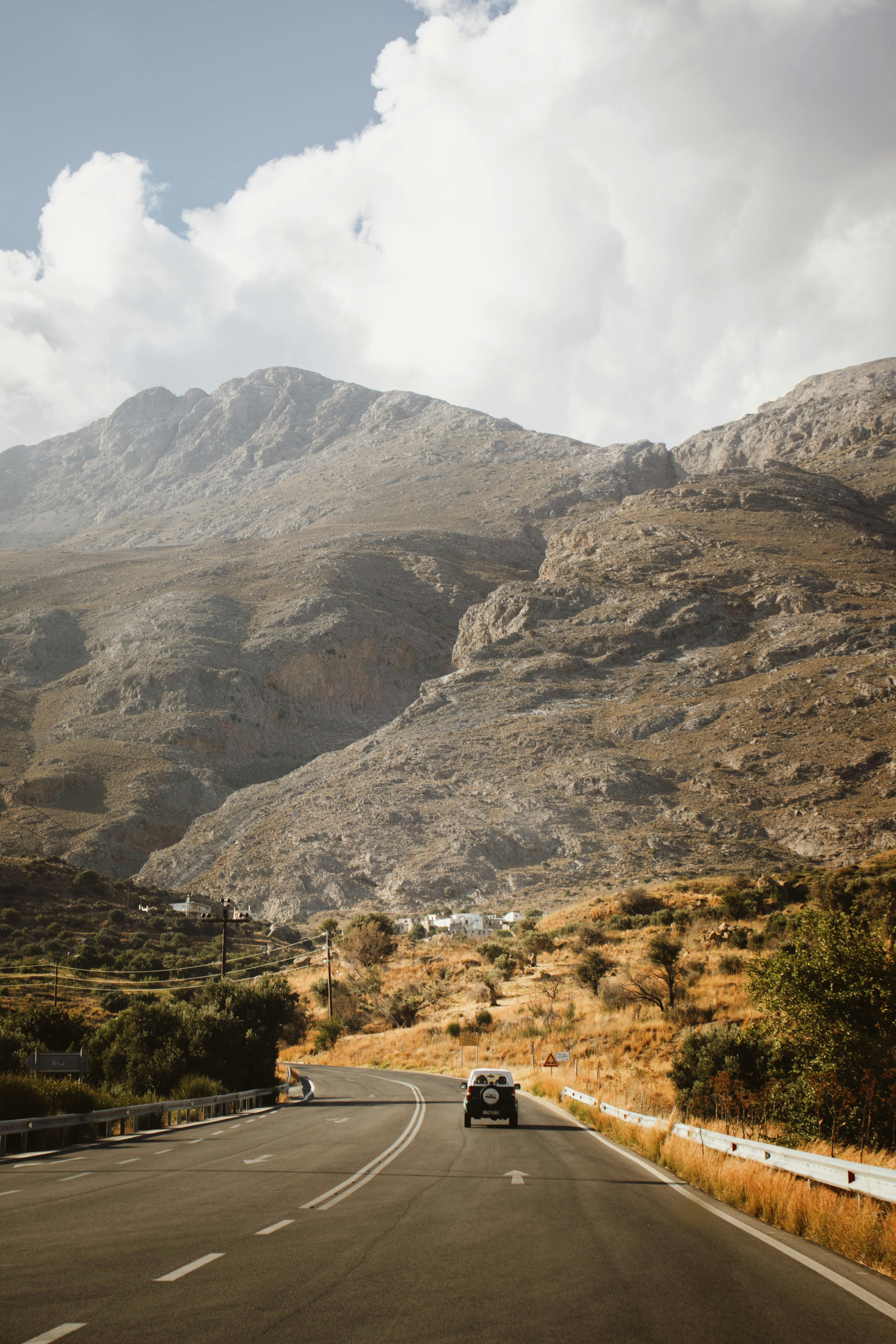 Explore a picturesque road winding through Crete's rugged mountain landscape under a bright summer sky.