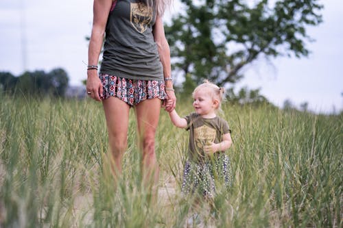 Woman Standing and Holding Hand of Baby Near Green Field