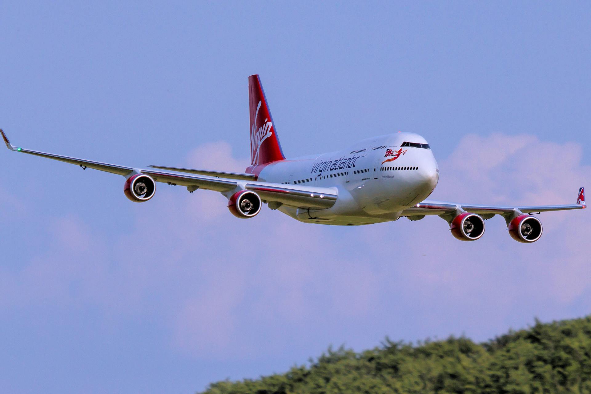 Virgin Atlantic Boeing 747 cruising through clear blue sky over lush greenery.