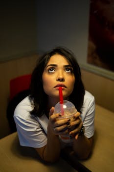 Young woman indoors holding bubble tea, gazing upwards thoughtfully.