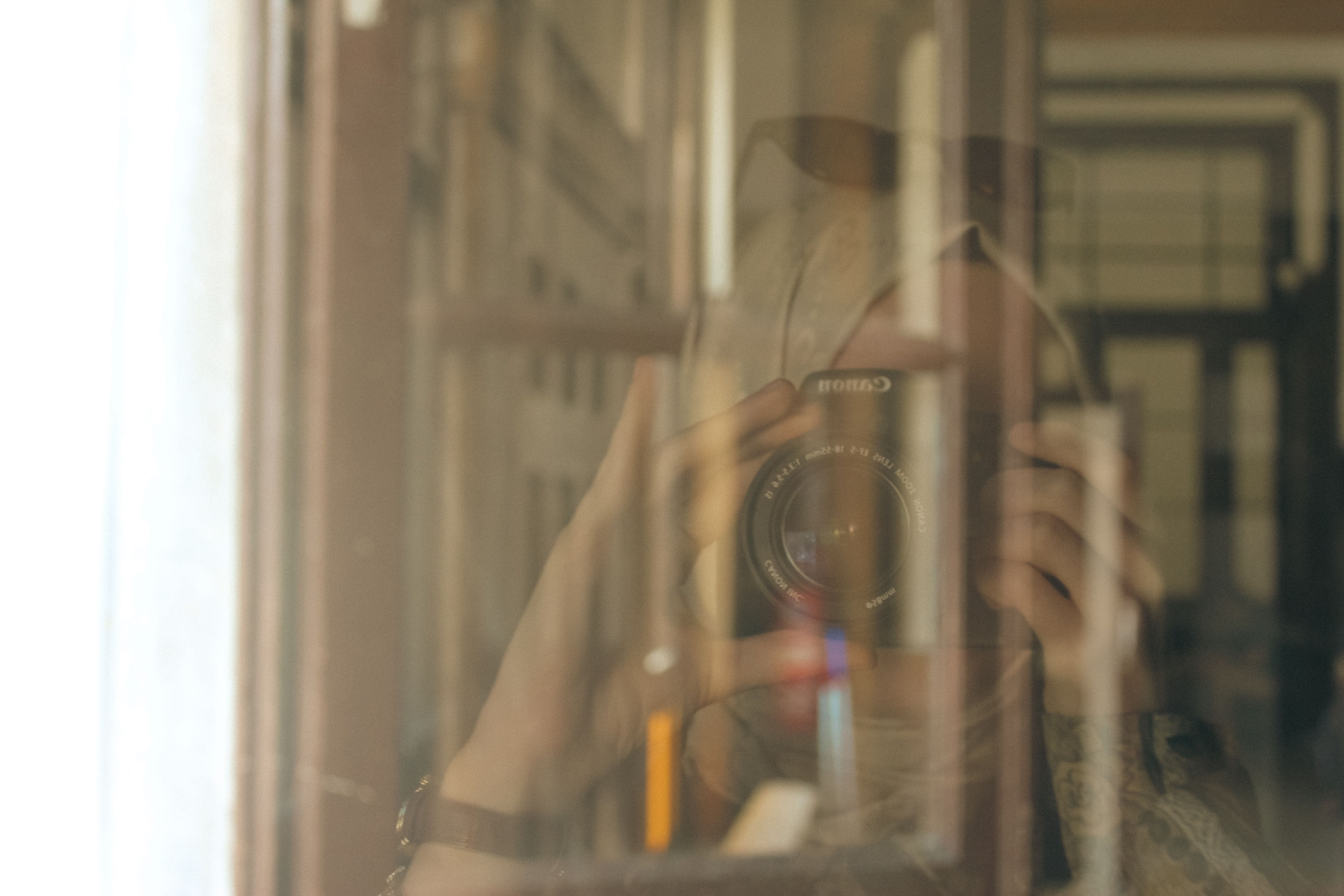 A reflective portrait capturing a photographer with a camera through a glass pane, blending interior and exterior views.