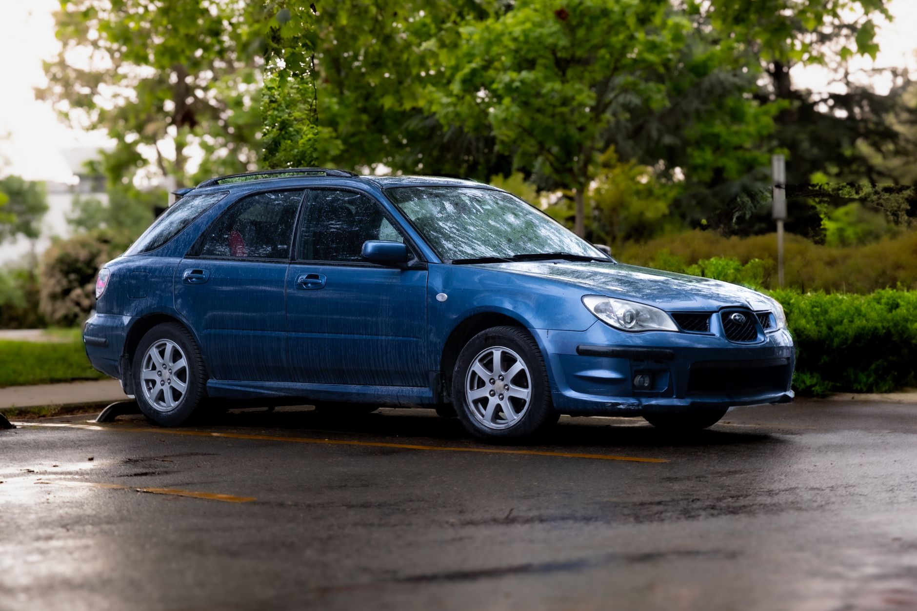 A blue Subaru station wagon parked outside on a rainy day, showcasing its design.