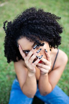 一位卷发的时尚女士在户外展示她复杂的美甲，同时用手微微遮住脸