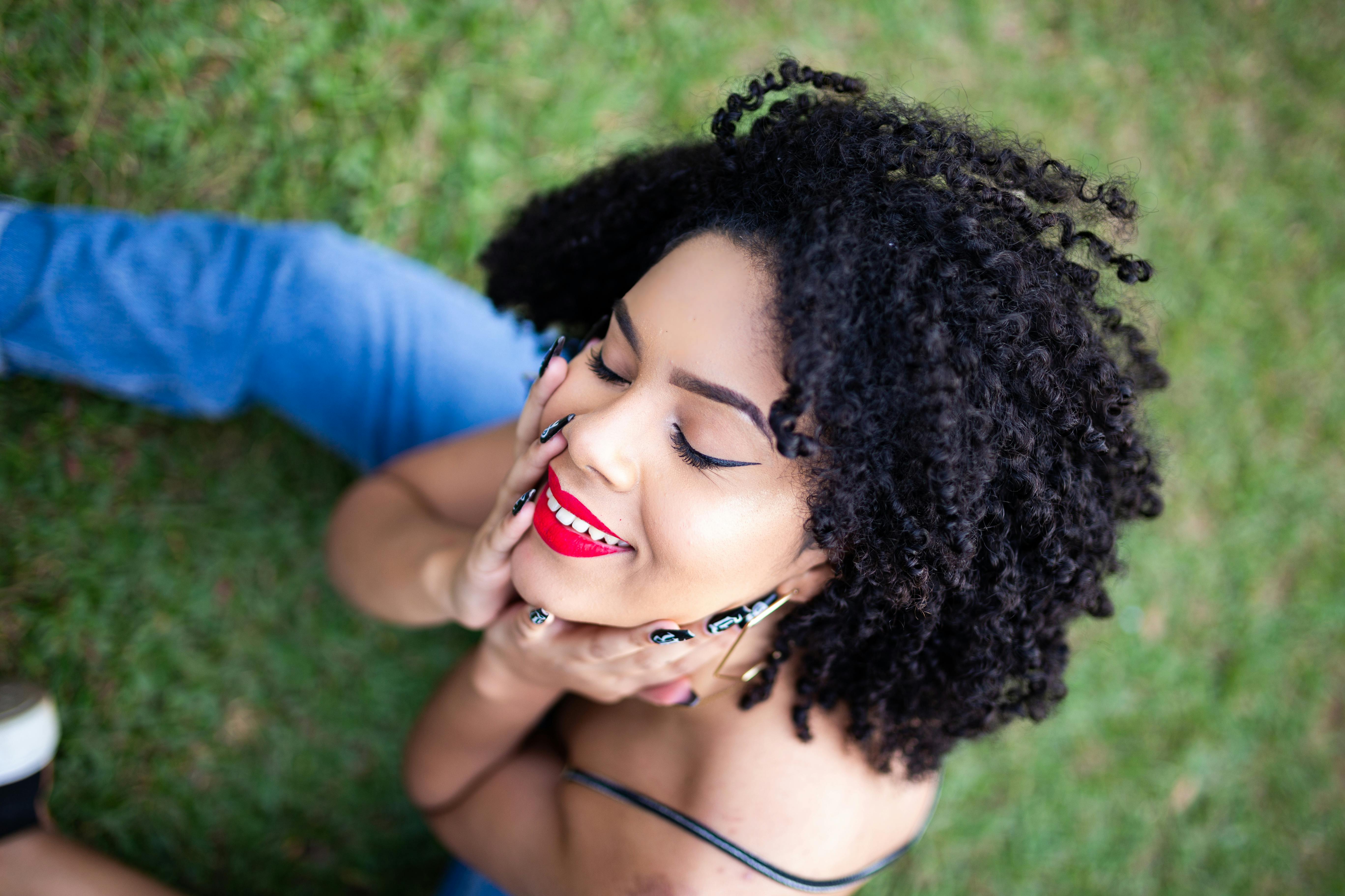 一位美丽的卷发女子涂着红色口红，在户外闭眼微笑摆着姿势