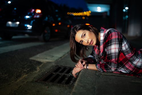 Photo of Woman in Plaid Shirt Lying Down on Curb at Night