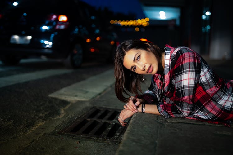 Photo Of Woman In Plaid Shirt Lying Down On Curb At Night