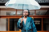 街头风格肖像中，一名穿着牛仔和服的男子撑着伞，伞上栖息着一只鸟