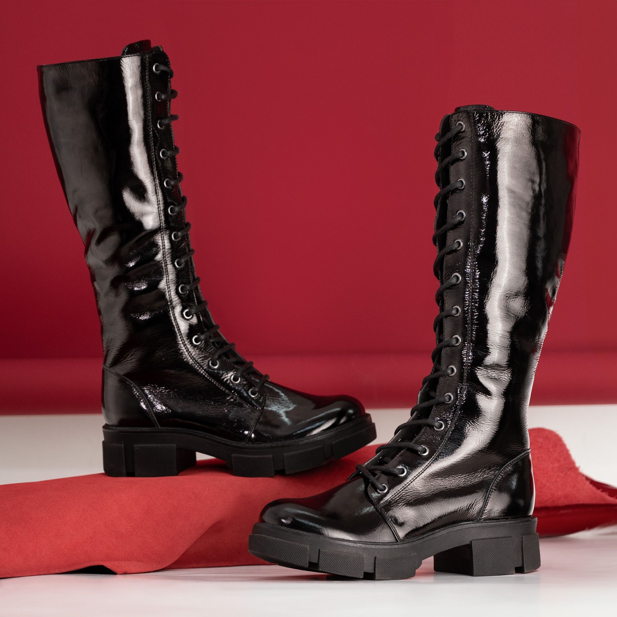 Sleek black boots with laces showcased against a vibrant red backdrop.