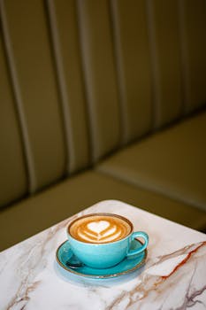 Close-up of a latte with beautiful art served in a blue cup on a marble table.