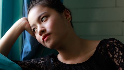 A contemplative woman in a lace dress gazes pensively by the window indoors.