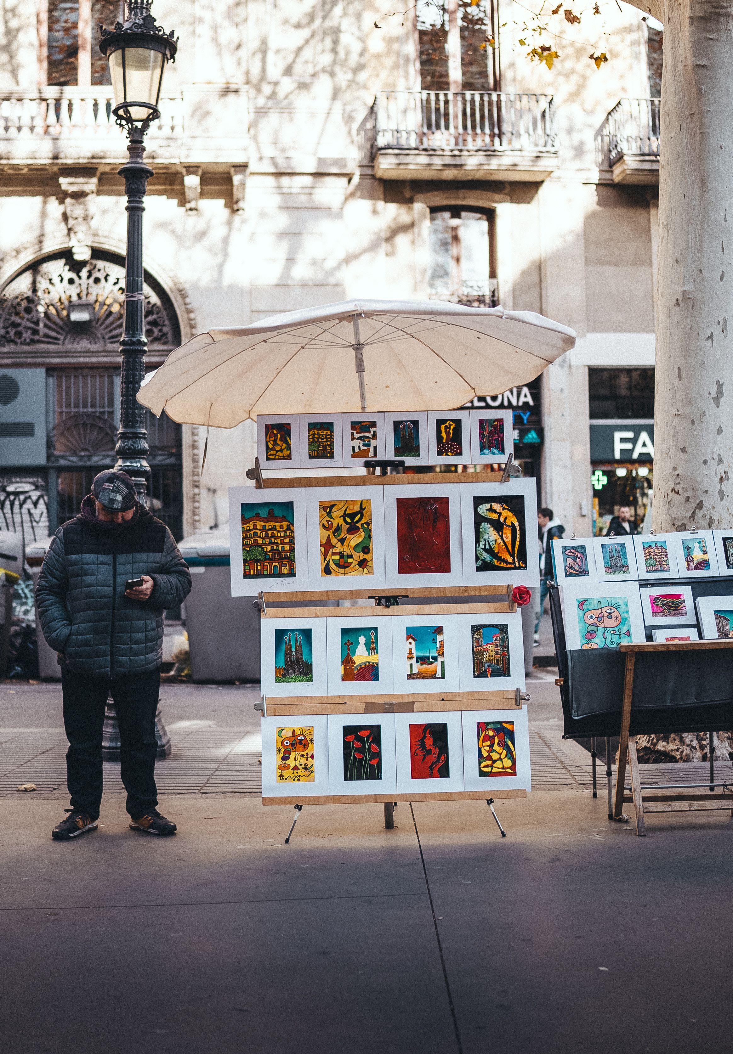 Art stall with colorful paintings on a busy urban street, offering unique handcrafted pieces for sale.
