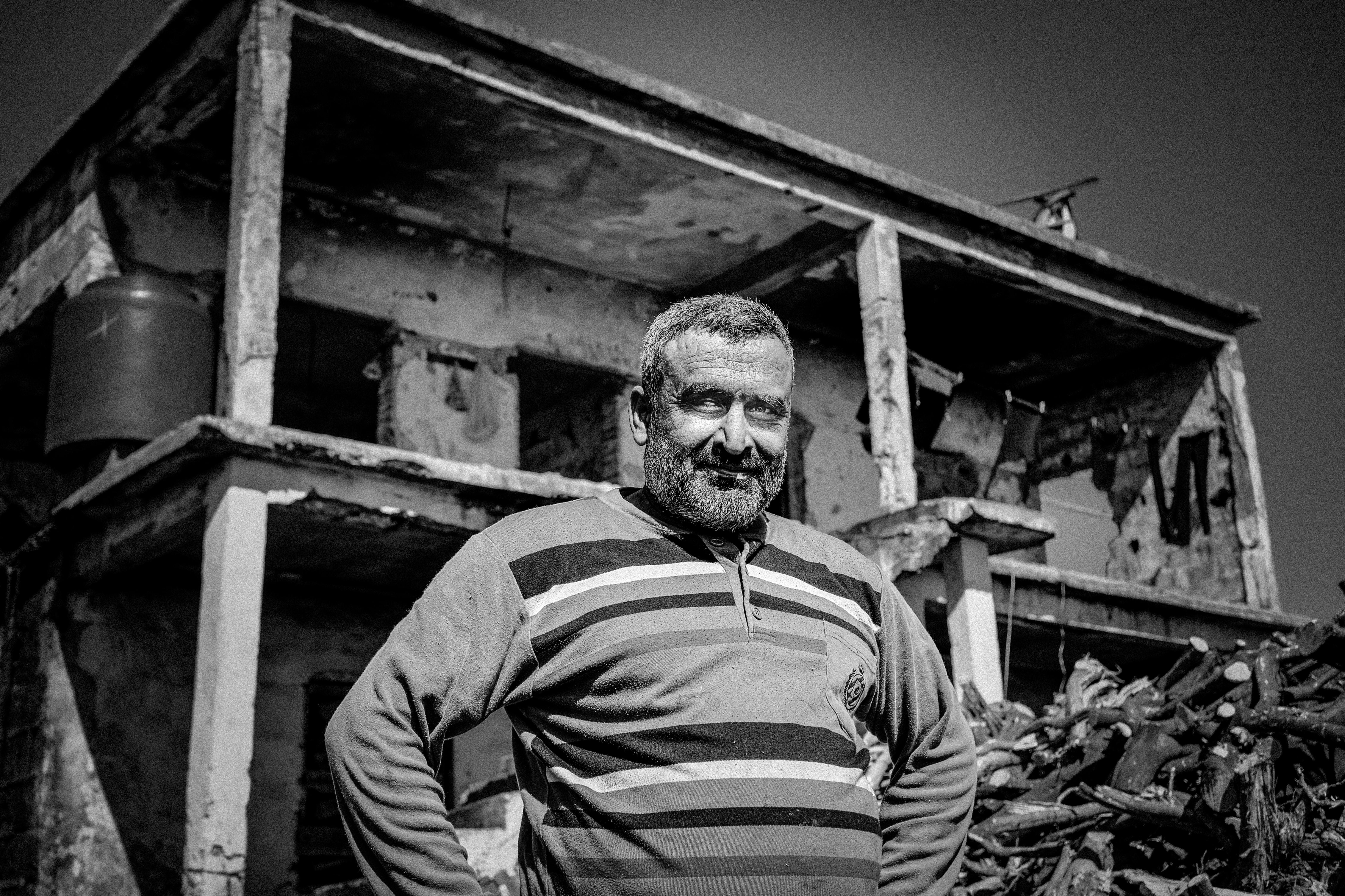 Black and white photo of a man standing in front of a decaying building in Adana, Turkey.