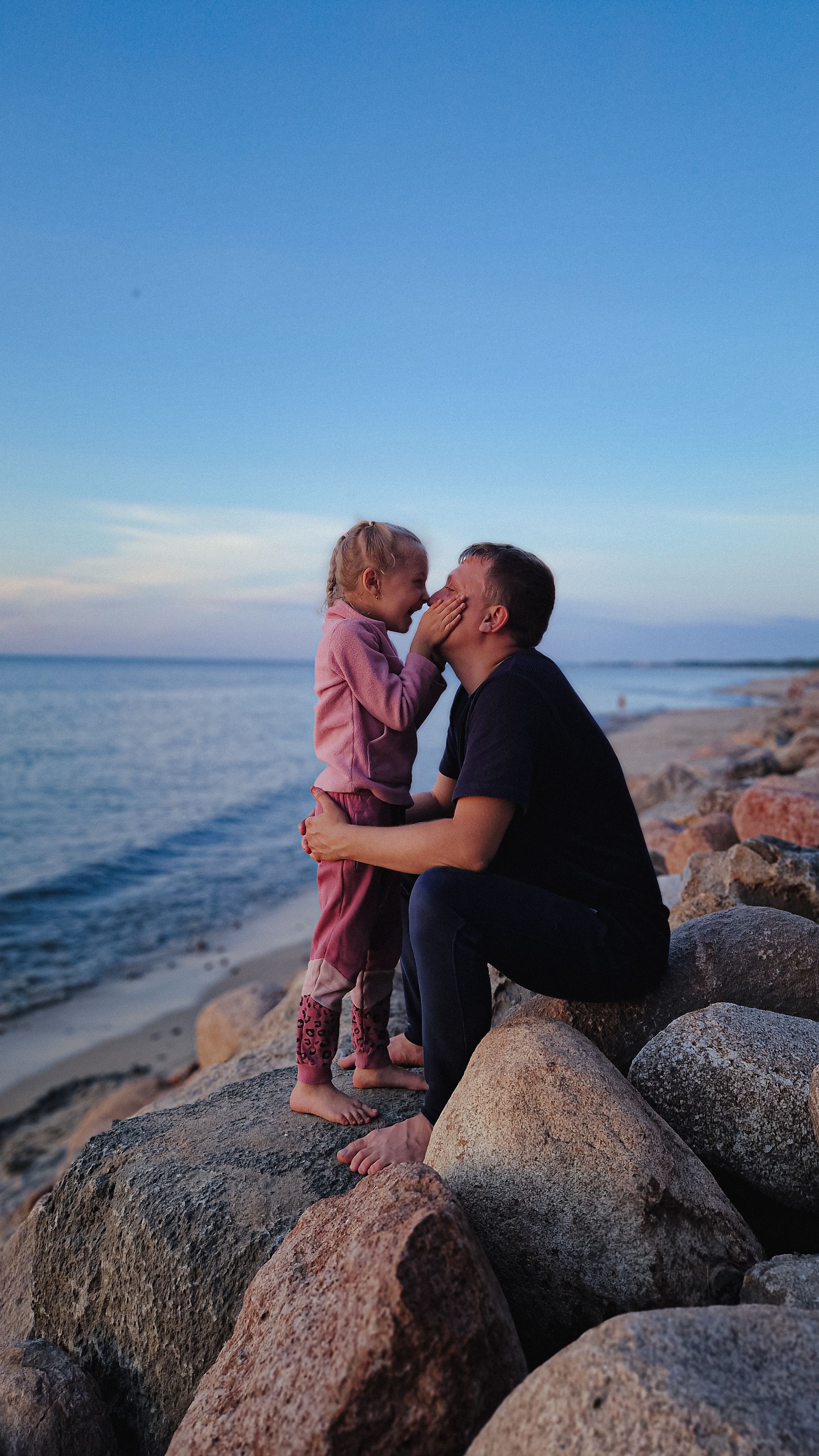 Father and daughter bonding on seaside rocks at sunset, embracing love and togetherness.