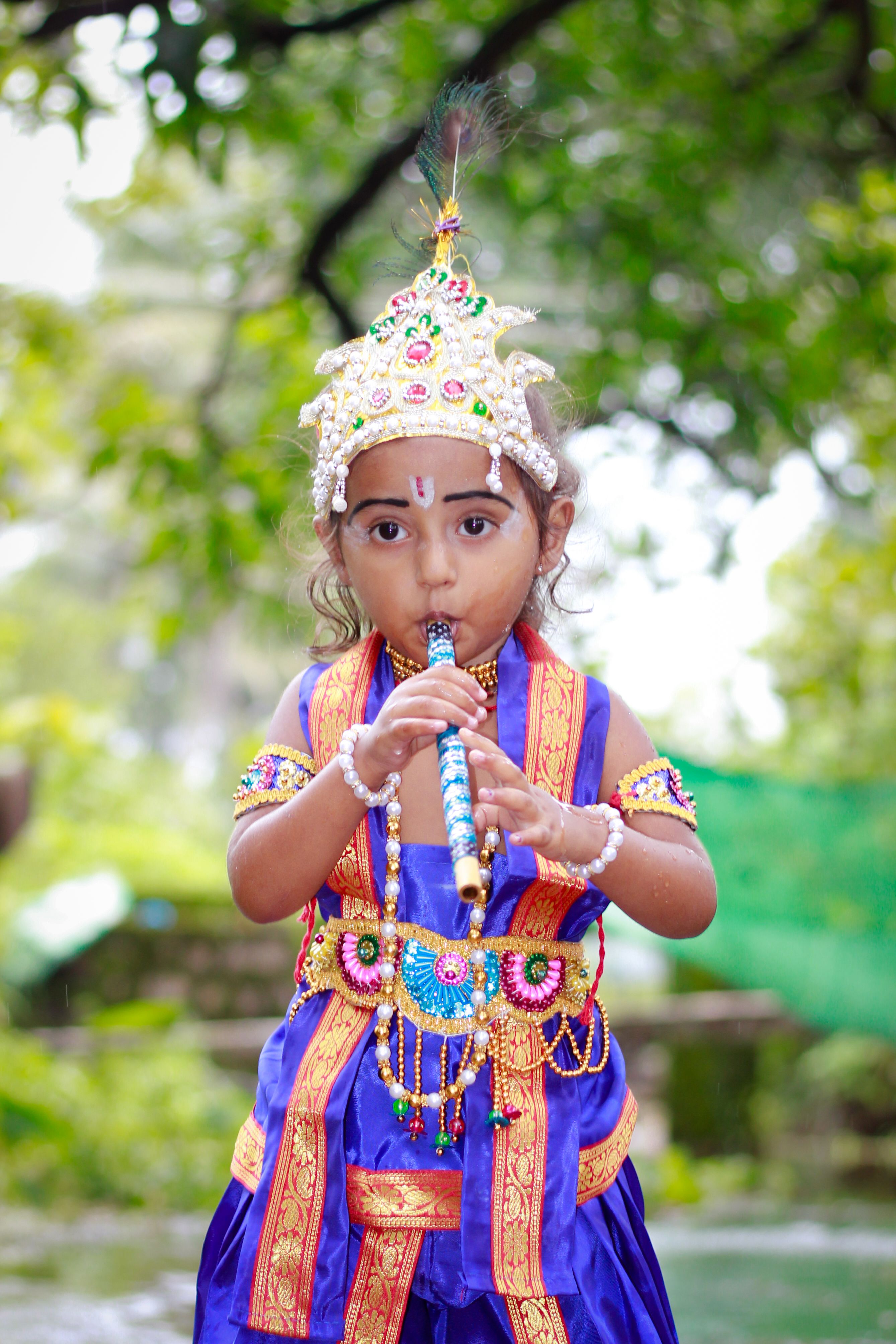 A child dressed in colorful traditional clothing plays the flute outdoors.