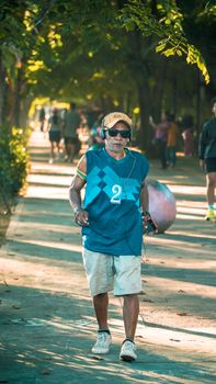 Senior man enjoying a walk in Pontianak park, wearing headphones and sunglasses.