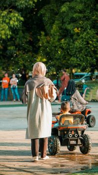 A mother and son enjoy a sunny day in the park with toy cars and playful activities. - Fotografer Sidoarjo