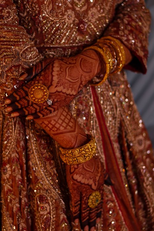 Free Close-up of an Indian bride's hands with henna, gold jewelry, and embroidered gown, showcasing cultural elegance. Stock Photo
