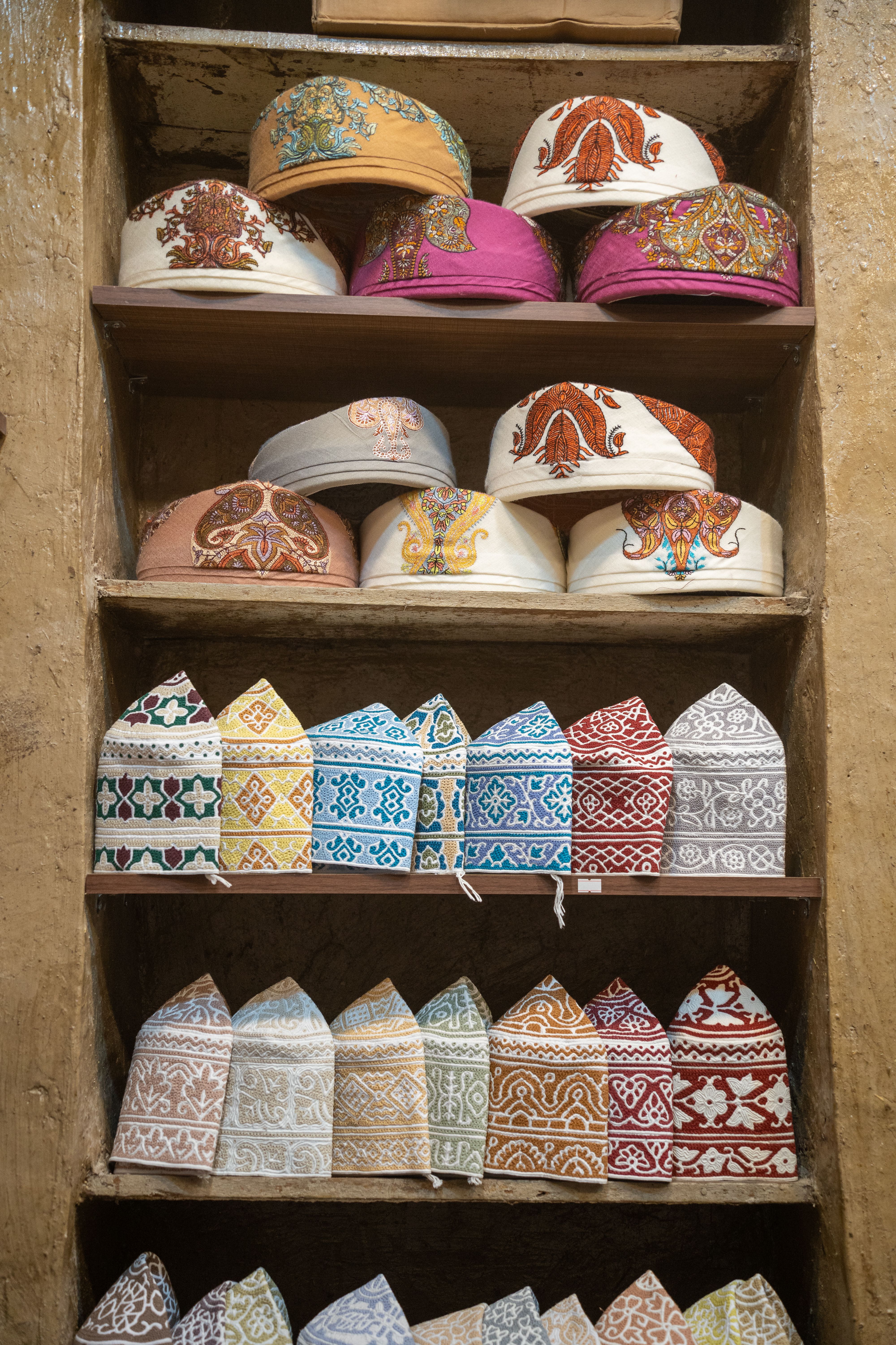Colorful Omani traditional caps stacked on wooden shelves in a market setting.