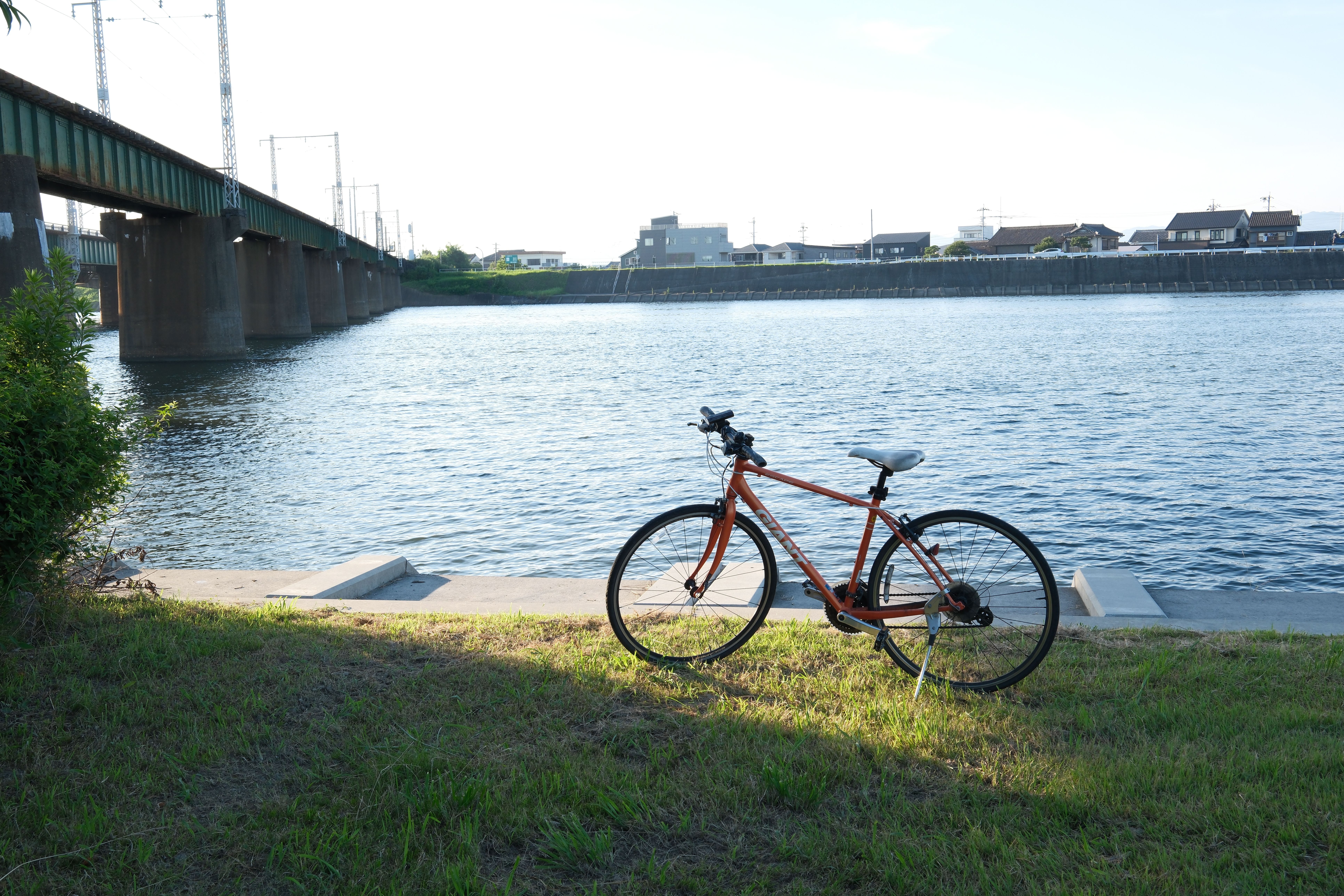 静かな川のそばに駐車された自転車の穏やかなイメージと背景に橋があります。