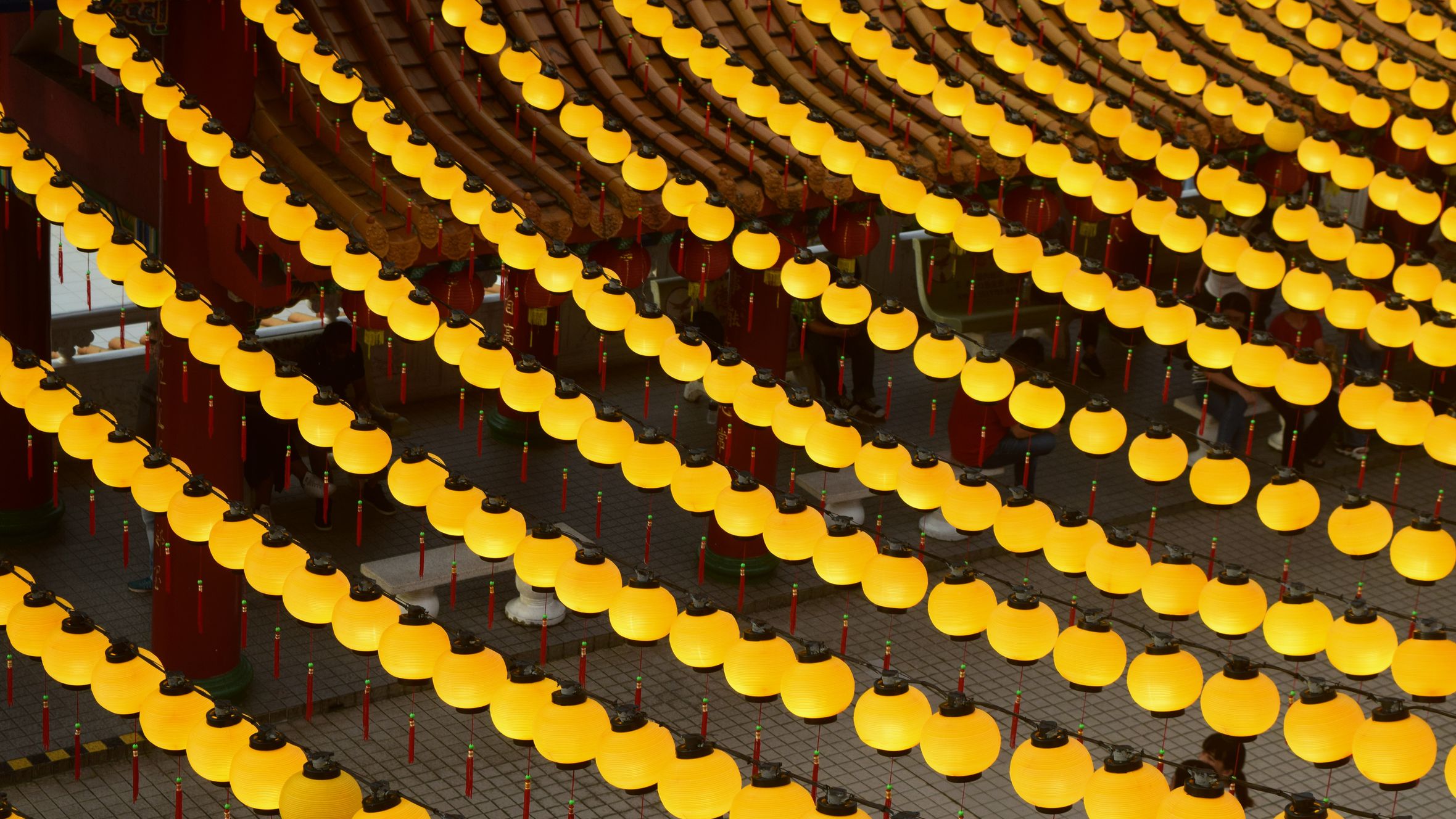 Rows of yellow lanterns illuminating a temple courtyard create a vibrant and festive atmosphere.