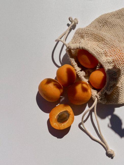 Close-up of fresh apricots spilling from a mesh bag highlighted by natural sunlight.