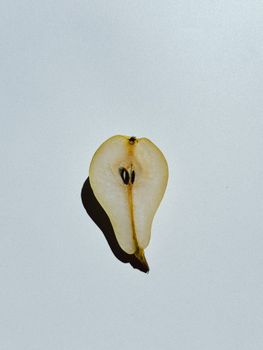 Sliced pear on a white background casting a shadow, minimalist still life.