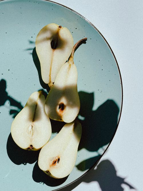 Free Artistic still life of pear halves casting shadows on a ceramic plate. Stock Photo