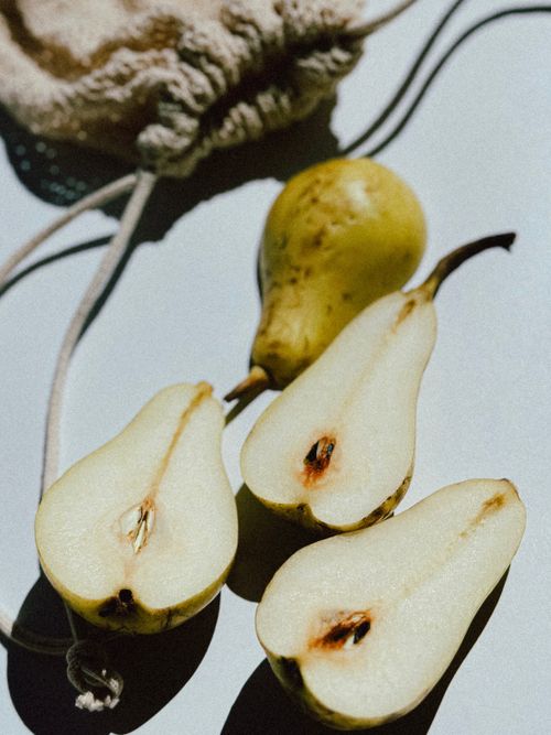 Free Sliced and whole pears artfully arranged in sunlight on a white surface with a string bag. Stock Photo