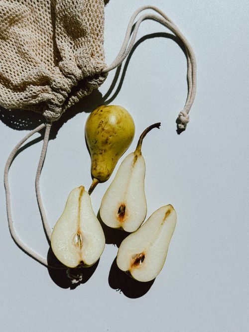 Free A minimalist still life featuring whole and sliced pears with a string bag on a white surface. Stock Photo