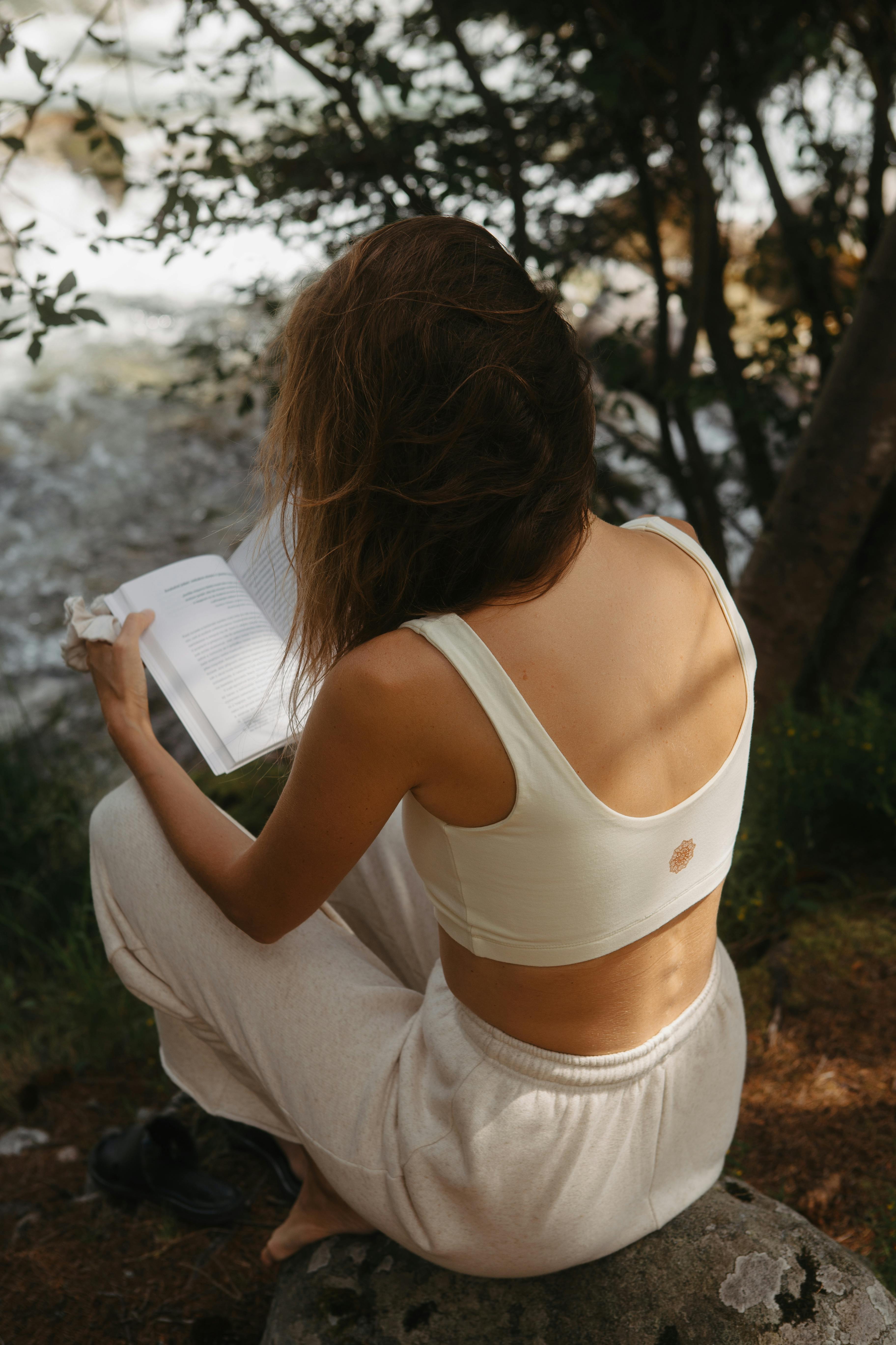 Woman sitting on a rock reading a book in a peaceful forest setting.