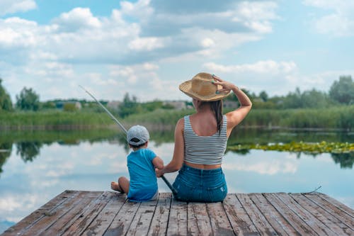 Woman and Boy Sitting on Dock Holding Fishing Rod