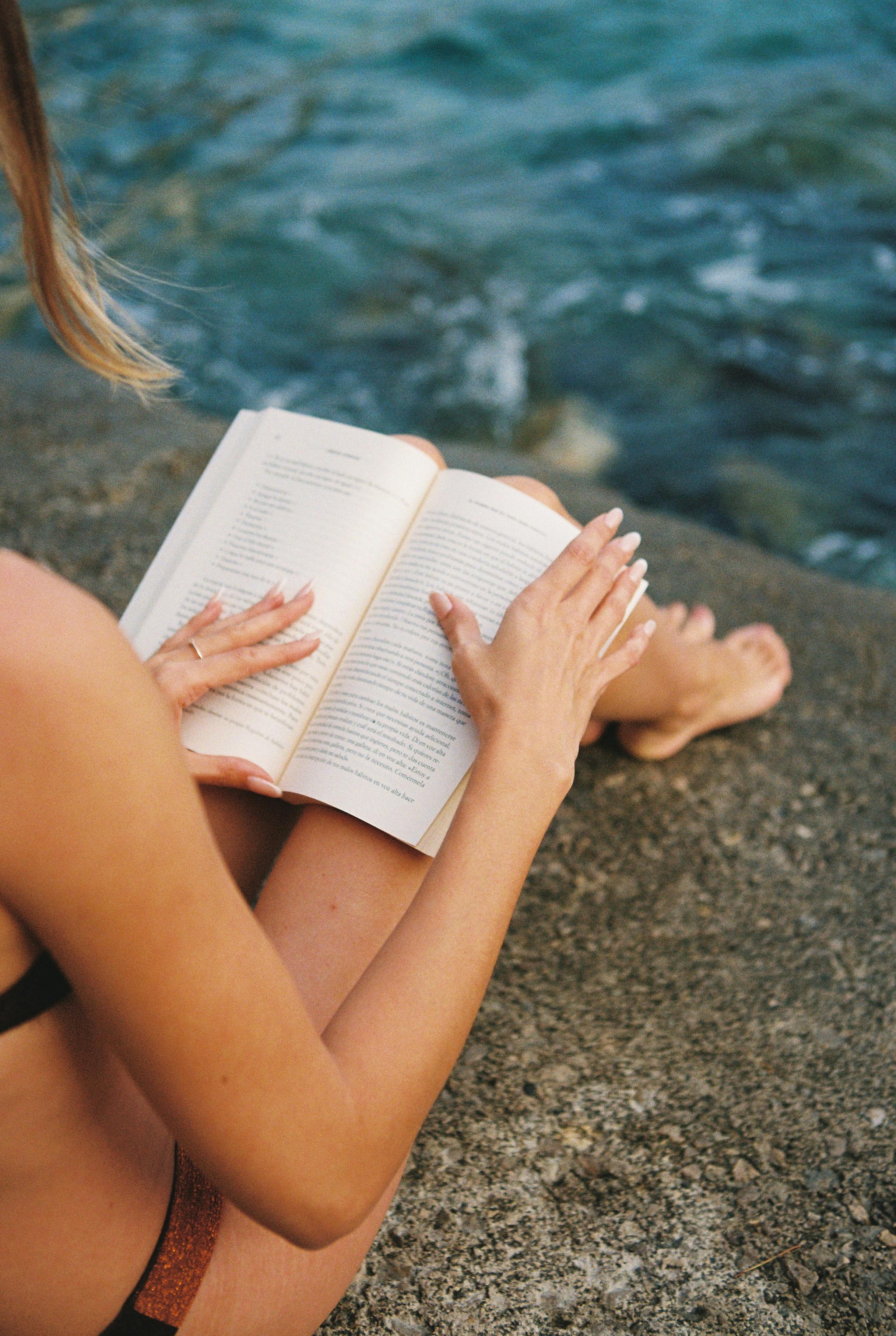 woman reading book sitting on rock above sea