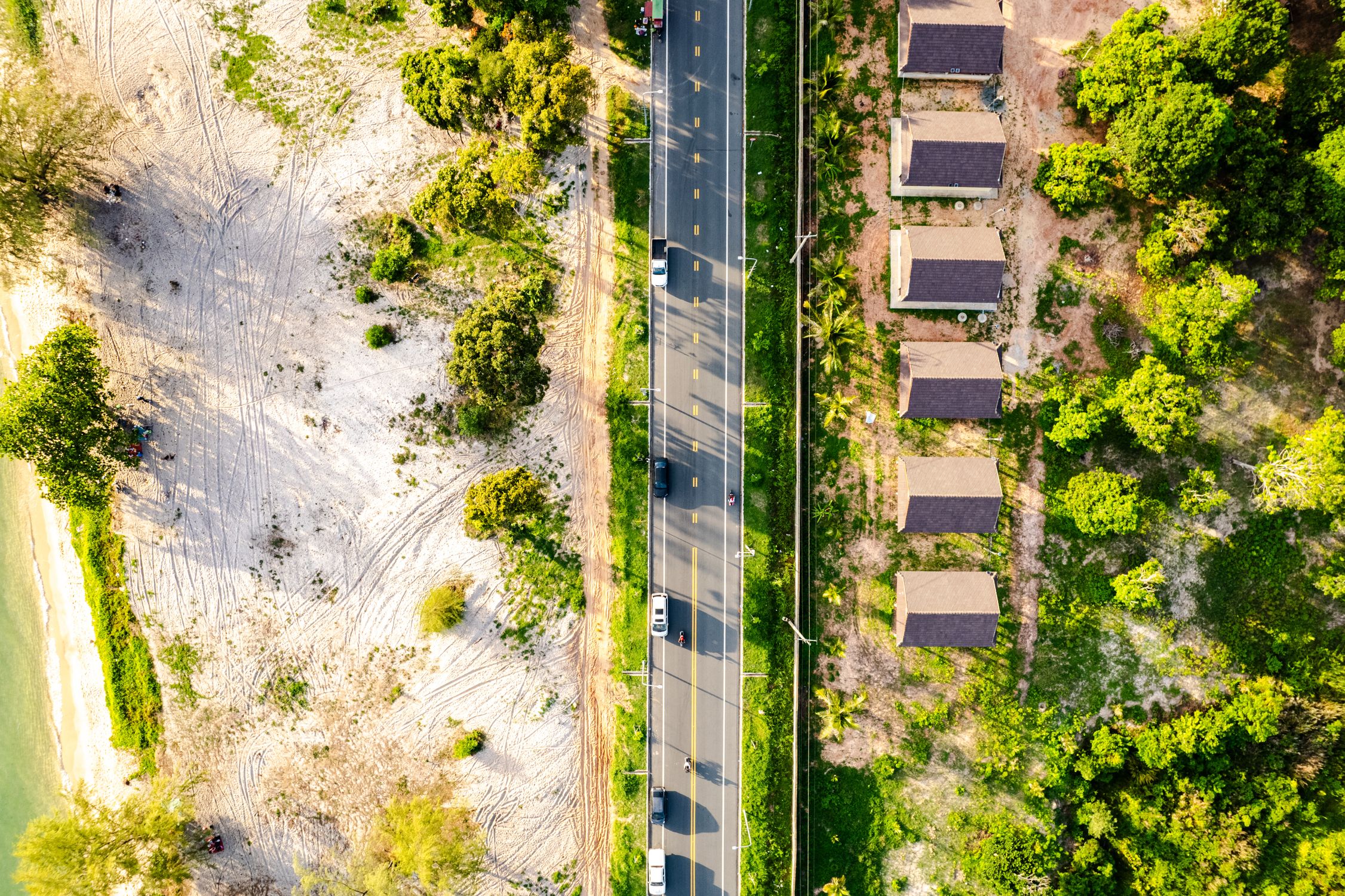 Drone shot of a coastal road between cottages and a sandy beach, highlighting nature and travel.