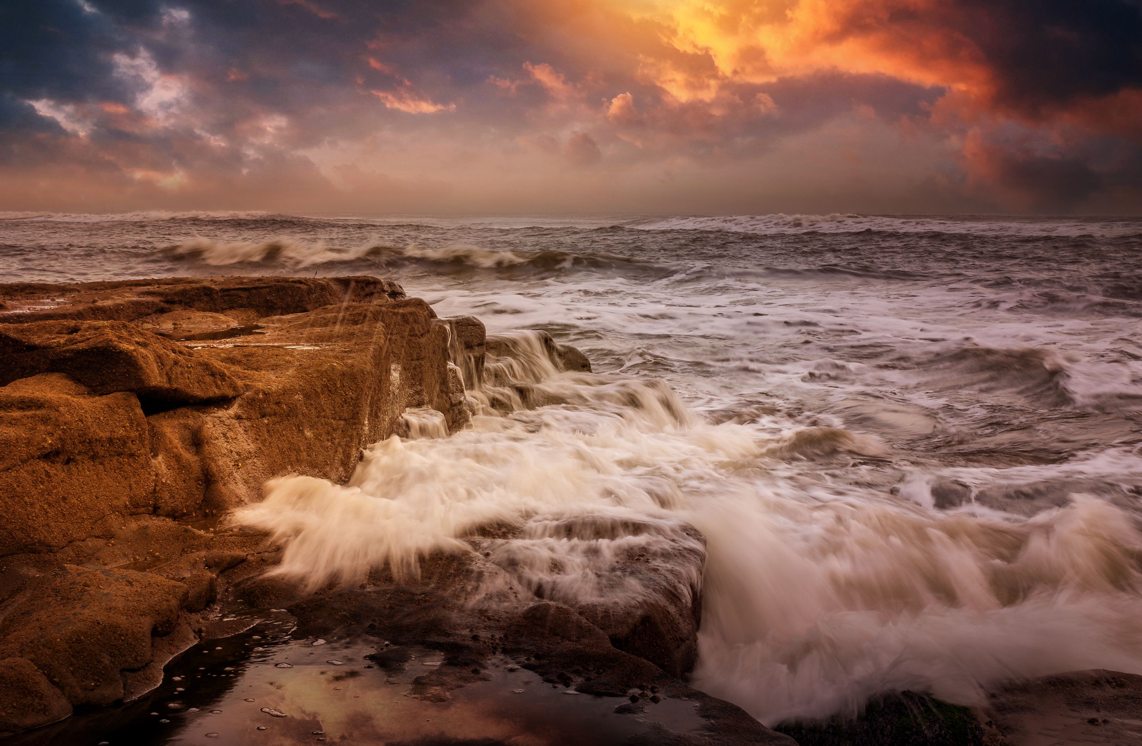 A sunset over the ocean with waves crashing on rocks · Free Stock Photo